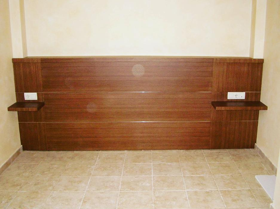 Cabezal de dormitorio a medida en madera oscura con mesillas suspendidas y enchufes integrados.