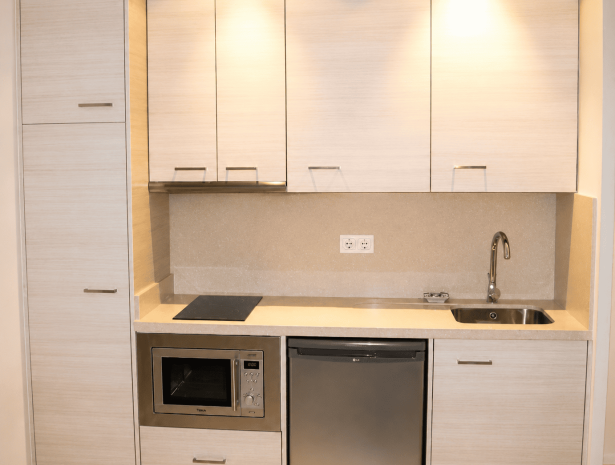Cocina compacta a medida en tonos claros con electrodomésticos integrados y soluciones de almacenamiento para espacios pequeños.