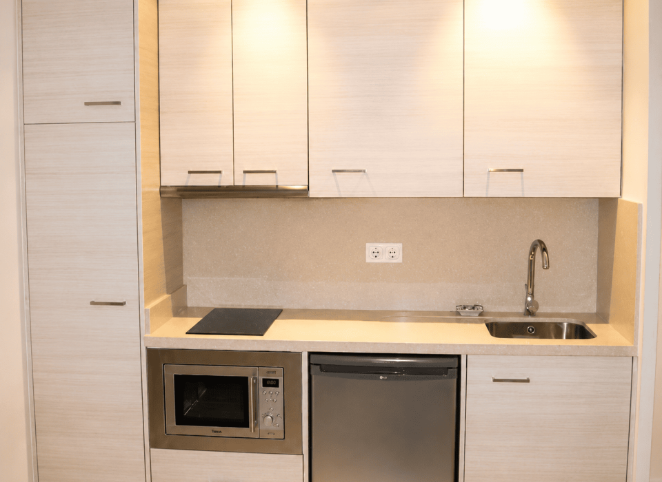 Cocina compacta a medida en tonos claros con electrodomésticos integrados y soluciones de almacenamiento para espacios pequeños.